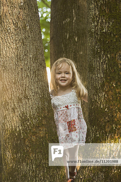Portrait of cheerful cute girl standing amidst trees at park
