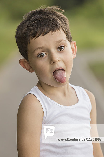 Portrait of boy sticking out tongue while standing at park