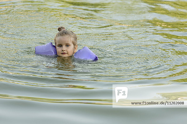 Portrait of cute girl wearing water wings swimming in lake