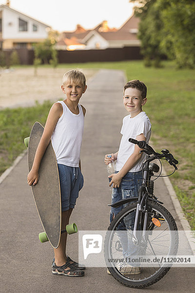 Smiling friends with skateboard and bicycle standing at park
