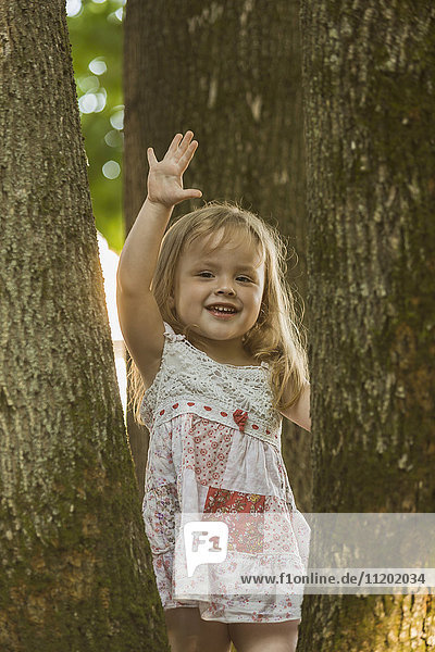 Portrait of cheerful girl gesturing while standing amidst trees at park