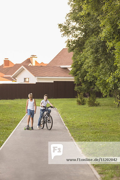 Friends with skateboard and bicycle at park against houses