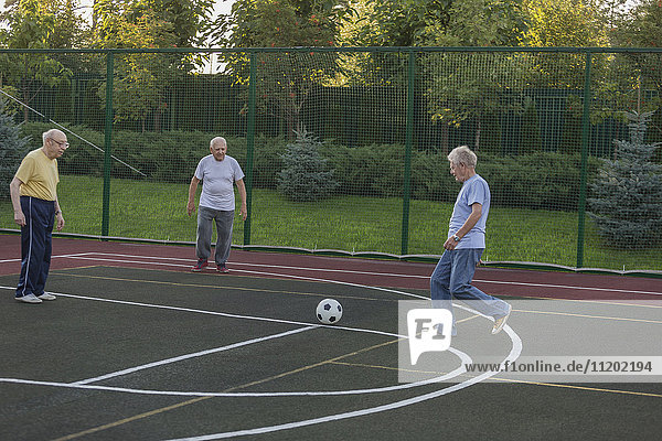 Seniorenfreunde spielen Fußball am Zaun auf dem Spielfeld