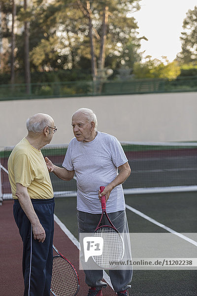 Ältere Freunde  die sich unterhalten  während sie Tennisschläger auf dem Platz halten.