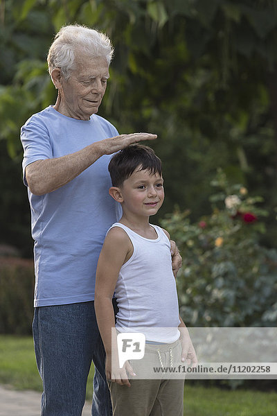 Lächelnder Großvater misst die Größe des Enkels beim Stehen im Park