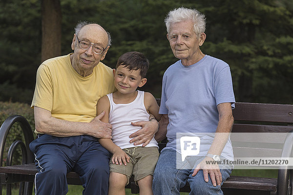 Portrait of smiling boy sitting with grandfathers at park bench