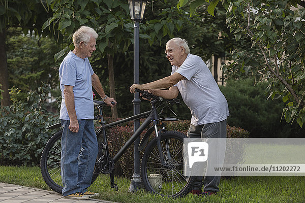 Smiling friends talking while standing by bicycle on field at park