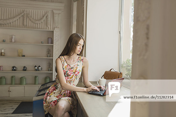 Junge Frau beim Sitzen am Fenster im Cafe mit Laptop