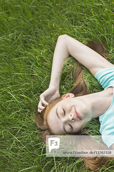 Hochwinkelansicht einer Frau  die mit geschlossenen Augen auf einem Grasfeld liegt.