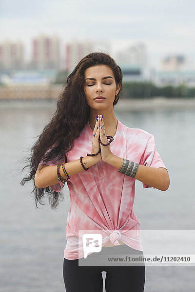 Junge Frau mit geschlossenen Augen praktiziert Yoga in Gebetsstellung gegen den Fluss