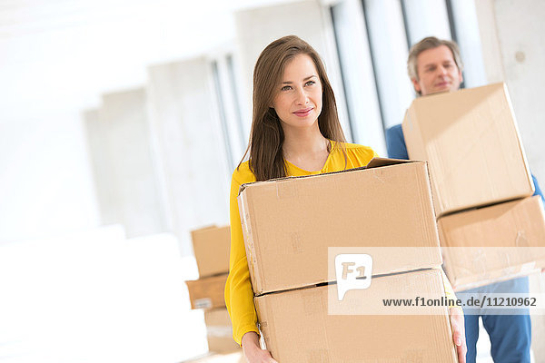 Young businesswoman with male colleague carrying cardboard boxes in new office