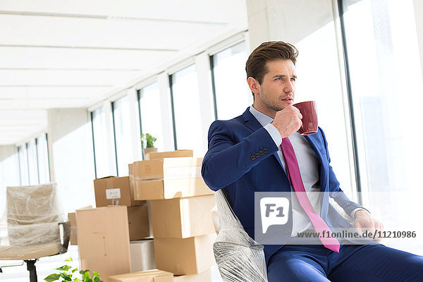 Porträt eines jungen Geschäftsmannes beim Kaffeetrinken mit Umzugskartons im Hintergrund im Büro