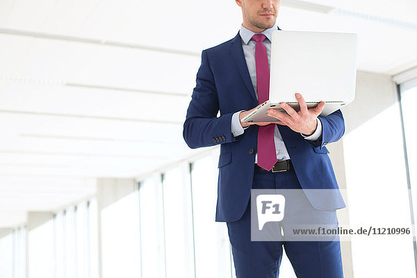 Midsection of young businessman using laptop while standing in new office