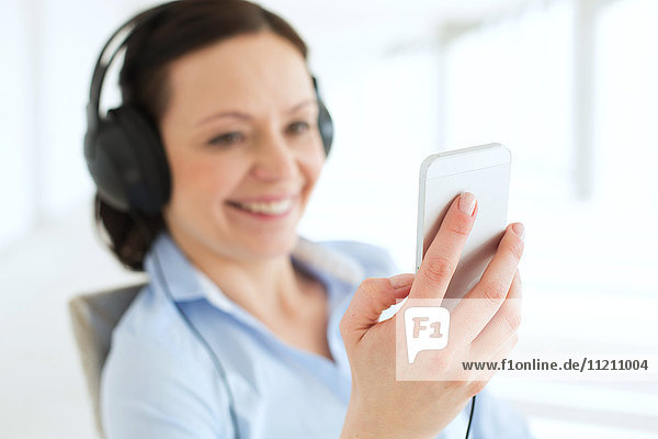 Smiling businesswoman listening music through smart phone in office