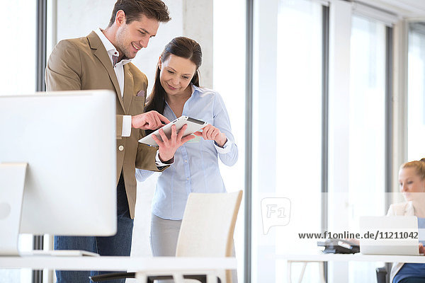 Business people using tablet computer with female colleague in background at office