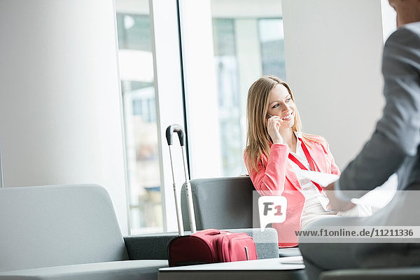 Smiling businesswoman using smart phone while sitting at lobby in convention center
