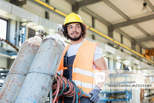 Young manual worker moving gas cylinders in metal industry