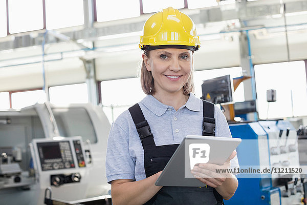 Porträt einer lächelnden Arbeiterin  die ein digitales Tablet in der Fertigungsindustrie benutzt