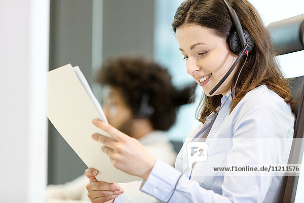 Young businesswoman wearing headset while reading document in office