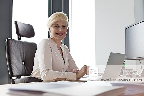 Portrait of smiling mature businesswoman sitting at desk in office