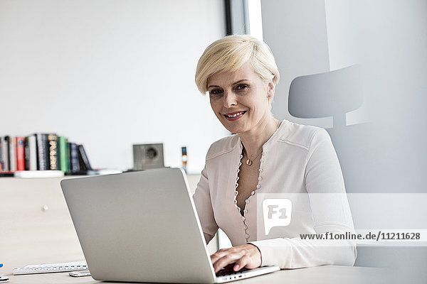Portrait of smiling mature businesswoman using laptop at desk in office