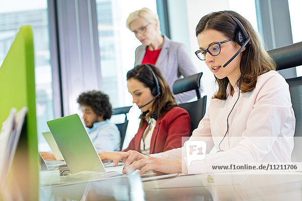Female customer service representative using laptop while colleagues in background at office