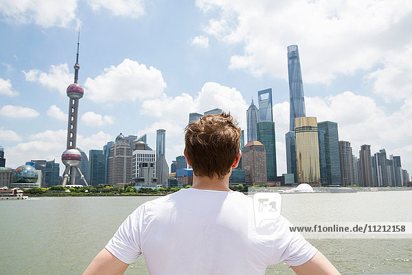 Rear view of man looking at Pudong skyline against cloudy sky