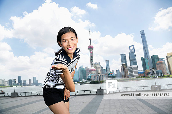 Portrait of happy woman gesturing while standing on promenade against Pudong skyline
