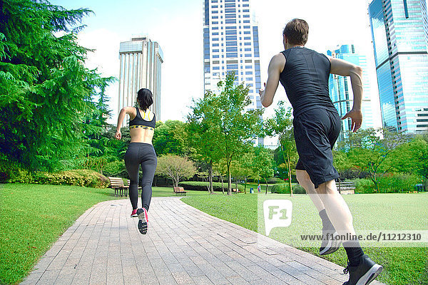 Healthy sports people trail running living an active life. Happy lifestyle couple of athletes training cardio together in summer outdoors. Multi-ethnic group Asian woman with handsome fit man trainer.