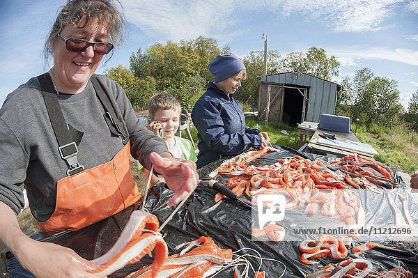 Young boy talks on a cell phone while adults filet and hang caught salmon Bristol Bay Alaska