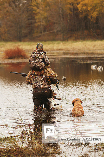 Father Carries Son Through Water With Dog While Duck Hunting