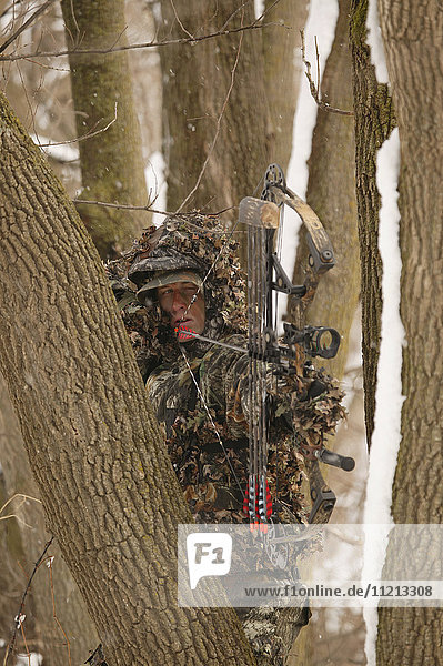 Male Bowhunter Draws Bow In Snow While Deer Hunting