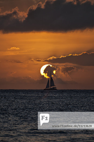 Silhouette eines Segelboots bei Sonnenuntergang unter glühender Sonne mit orangefarbenem Himmel und dramatischen Wolken; Hawaii  Vereinigte Staaten von Amerika