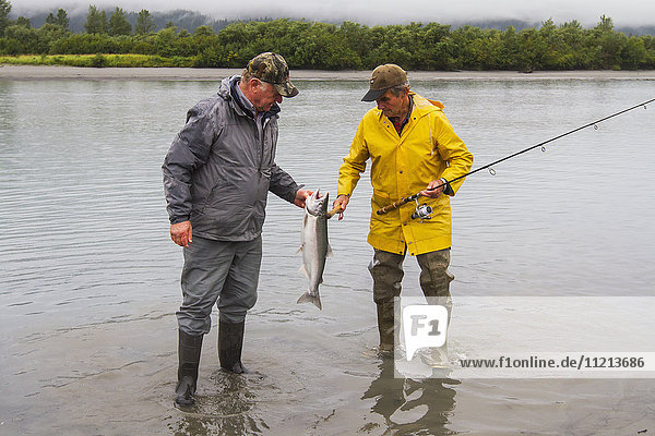 Ein befreundetes Paar betrachtet einen frisch gefangenen Silberlachs aus einem Fluss im Portage Valley im Sommer. Süd-Zentral-Alaska.