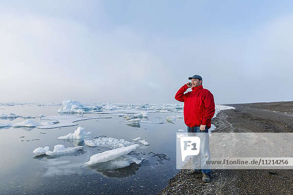 A man standing on the coast of the Arctic Ocean during a foggy sunset talks on his cell phone with sea ice floating in the background; Barrow; North Slope; Arctic Alaska; USA; Summer