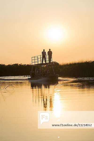 Silhouette von Menschen auf einem Boot bei Sonnenuntergang; Botswana'.
