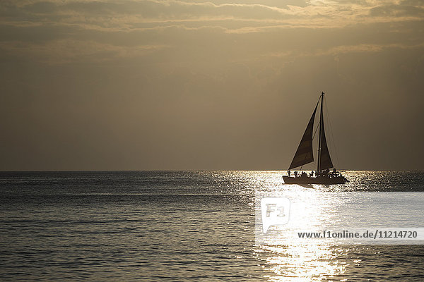 Ein Segelboot segelt vor Waikiki Beach bei Sonnenuntergang; Honolulu  Oahu  Hawaii  Vereinigte Staaten von Amerika'.