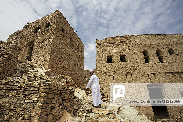Mann in Disdash vor den Ruinen des traditionellen in verlassenen alten Dorf