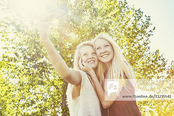 'Two sisters having fun outdoors in a city park in autumn and taking selfies of themselves; Edmonton  Alberta  Canada'