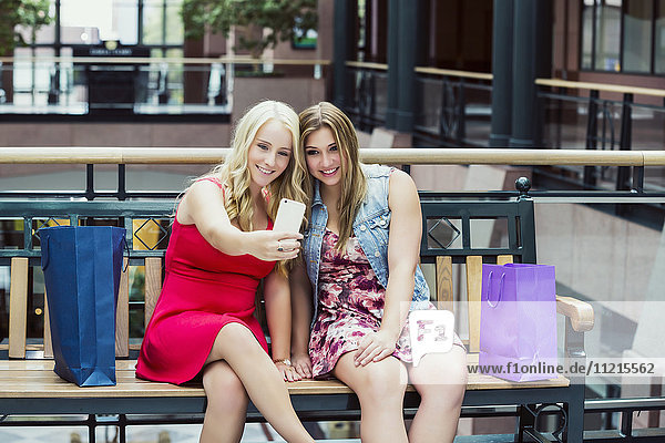'Two beautiful young women taking a break to take a selfie while out shopping together in an indoor mall; Edmonton  Alberta  Canada'