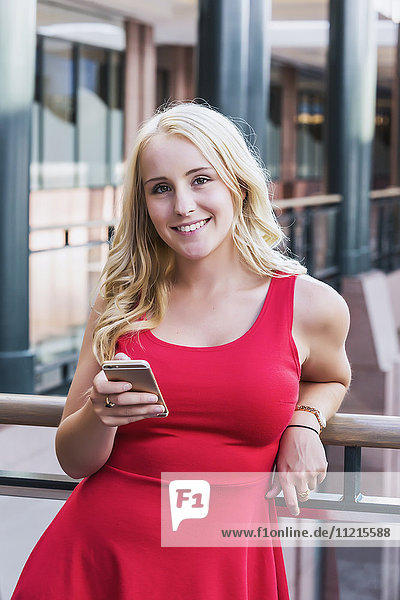 Eine hübsche junge Geschäftsfrau aus dem Millennium schreibt in einer Pause in einem Bürokomplex eine SMS und schaut in die Kamera; Edmonton  Alberta  Kanada .
