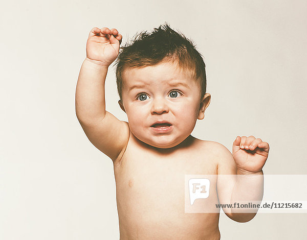 'Baby boy with his arm raised and a distressed look on his face against a white background; Saskatchewan  Canada'