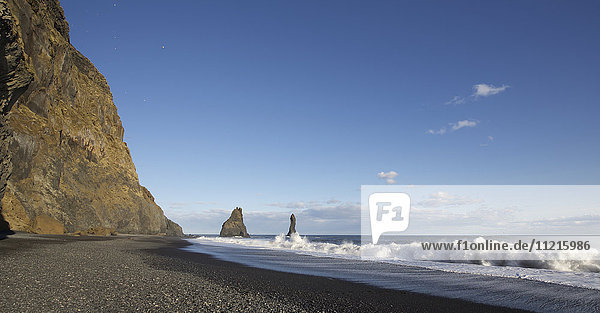 Wellen brechen am schwarzen Sandstrand mit riesigen Offshore-Stapelsäulen