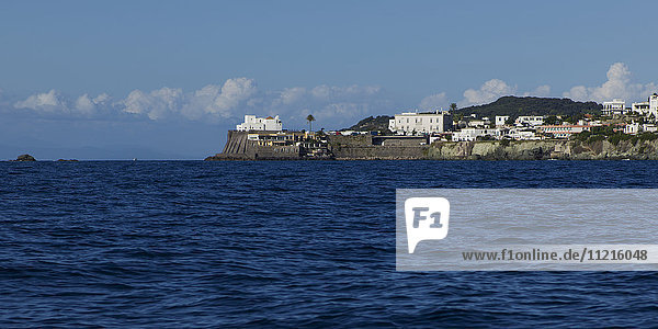 Insel Ischia mit Mauern entlang der Uferpromenade und weißen Gebäuden auf dem Vorgebirge; Ischia  Italien'.