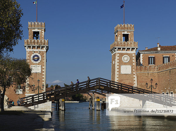 Fußgänger  die über eine Brücke mit einer Spitze und zwei Türmen mit Fahnen im Hintergrund gehen; Venedig  Italien
