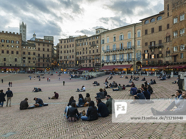 Spaziergänger und sitzende Menschen auf einem Stadtplatz; Siena  Italien