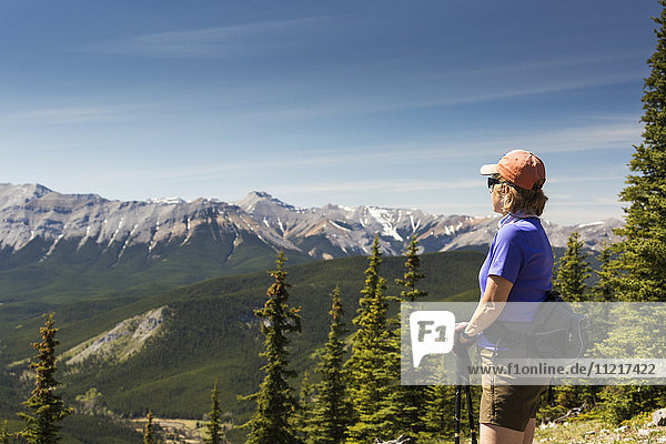 Wanderin mit Blick auf eine Bergkette in der Ferne  darunter ein Tal mit blauem Himmel und Wolken  Kananaskis Country; Alberta  Kanada'.