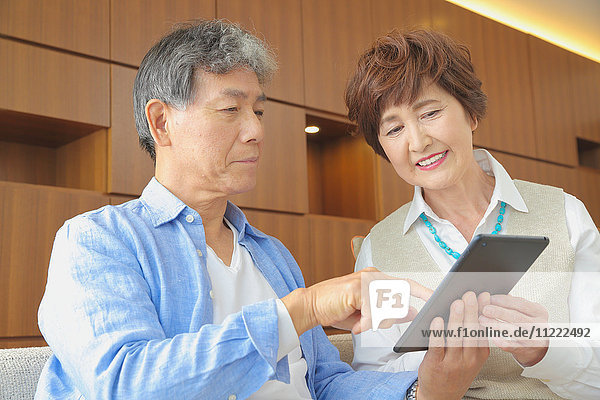 Fashionable Japanese senior couple with tablet on sofa