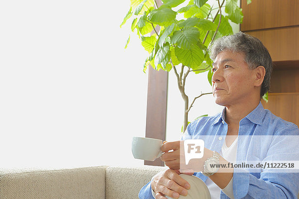 Modischer japanischer älterer Mann mit einer Tasse Kaffee auf dem Sofa