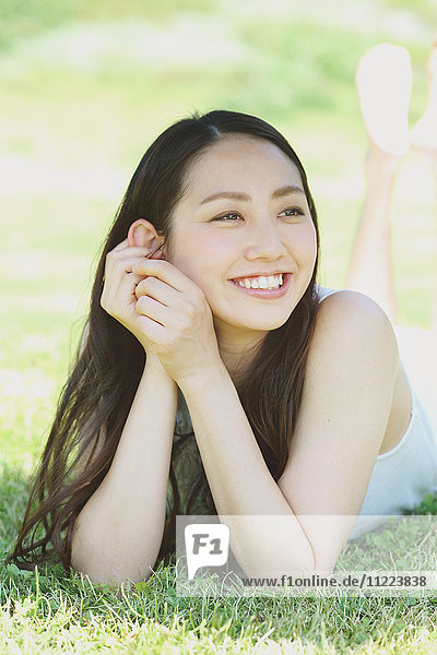 Porträt einer jungen japanischen Frau  die auf grünem Gras liegt